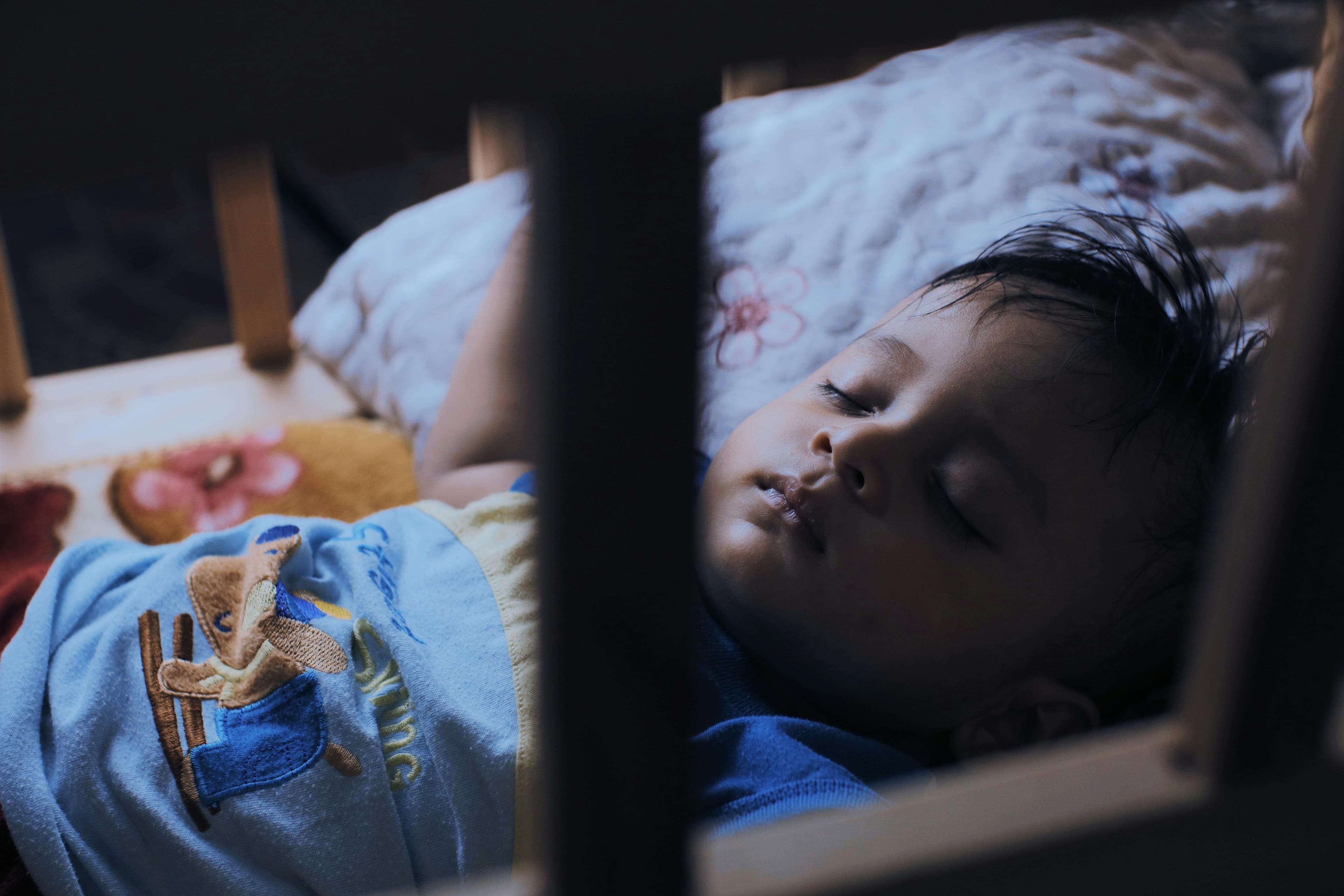 A baby rubbing their eyes while lying in a crib