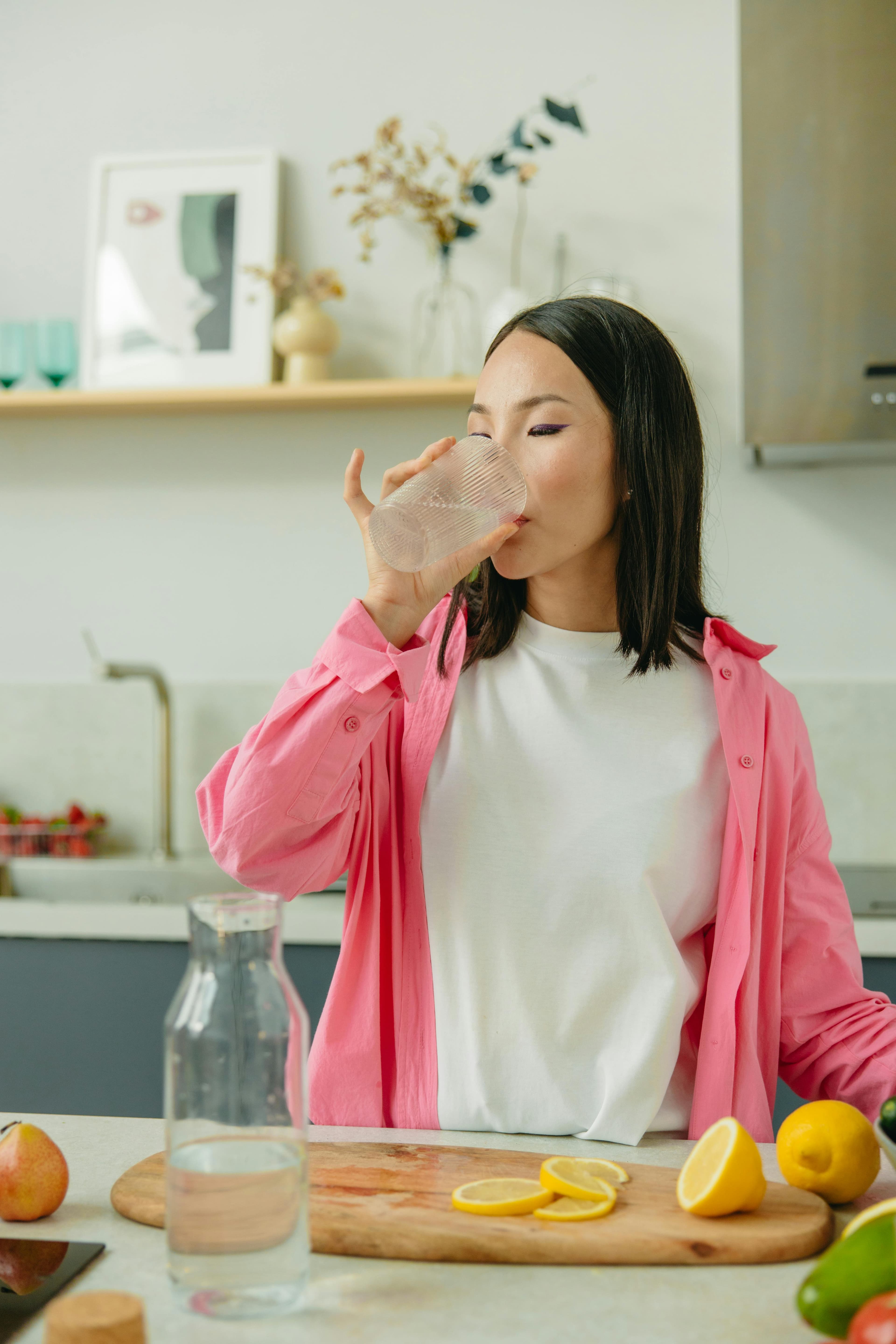 Person drinking water from a glass, surrounded by fresh fruits